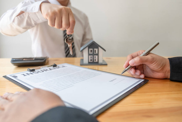 Makler übergibt dem neuen Eigentümer den Hausschlüssel nach Abschluss der Unterzeichnung gemäß Vereinbarung Anmietung eines Hauses und Kauf einer Hausversicherung. - Foto, Bild