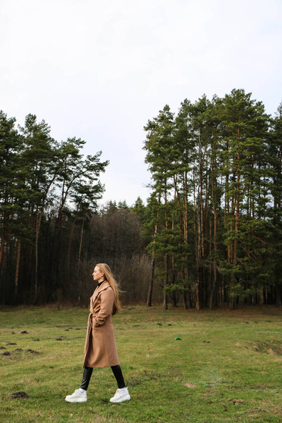 beautiful girl, blonde with long hair, walks in the spring near the forest in a brown coat., serenity and freedom - Valokuva, kuva