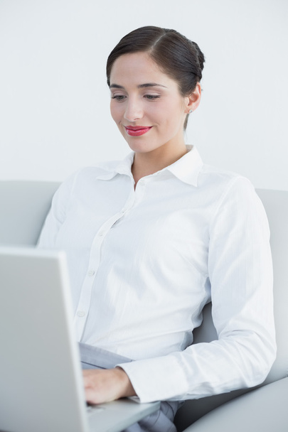 Smiling well dressed woman using laptop on sofa - Foto, imagen