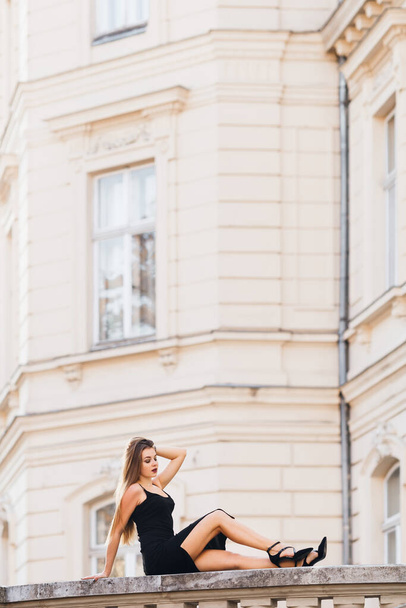 建物の背景に黒いドレスの美しいポーズの女の子。プロフィール. - 写真・画像