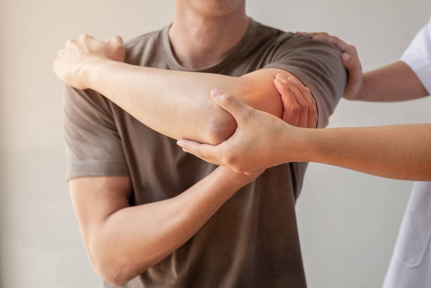 Female physiotherapists provide assistance to male patients with elbow injuries examine patients in rehabilitation centers. Physiotherapy concepts. - Photo, image