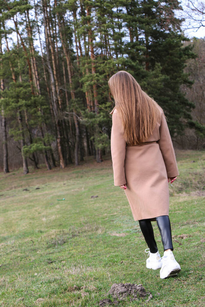 bella ragazza, bionda con i capelli lunghi, cammina in primavera vicino alla foresta in un cappotto marrone., serenità e libertà
 - Foto, immagini