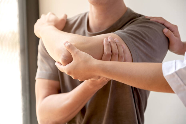 Female physiotherapists provide assistance to male patients with elbow injuries examine patients in rehabilitation centers. Physiotherapy concepts. - Foto, immagini