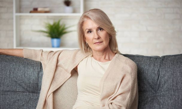 Portrét krásné starší blondýny sedí na pohovce doma - Fotografie, Obrázek