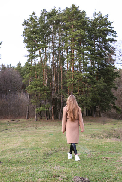 beautiful girl, blonde with long hair, walks in the spring near the forest in a brown coat., serenity and freedom - Foto, immagini
