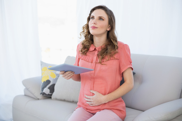 Thinking pregnant woman holding her tablet - Foto, Bild