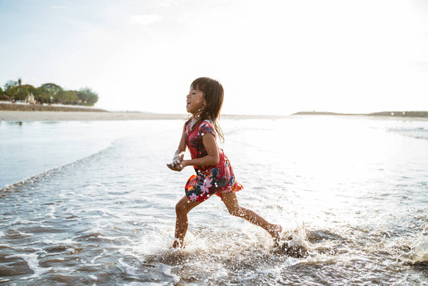 Little girl running on the beach while playing water - Foto, Imagen