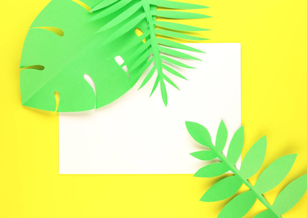 various tropical leaves with a white sheet of paper sunglasses on a yellow background, top view. exotic background with paper green leaves - Photo, image