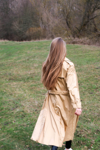 beautiful girl, blonde with long hair, walks in the spring near the forest in a brown coat., serenity and freedom - Φωτογραφία, εικόνα