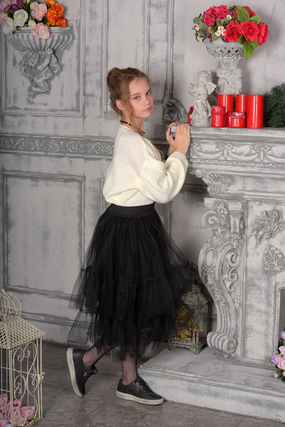 beautiful girl in a white sweater and black skirt by the fireplace - Foto, imagen