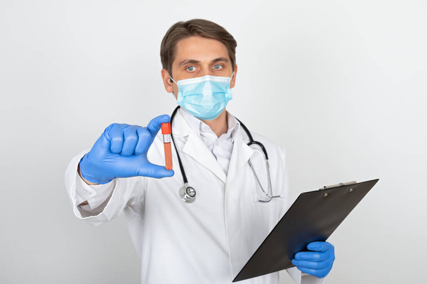 Young male doctor with surgical mask and gloves holding a blood sample on white background - Foto, immagini