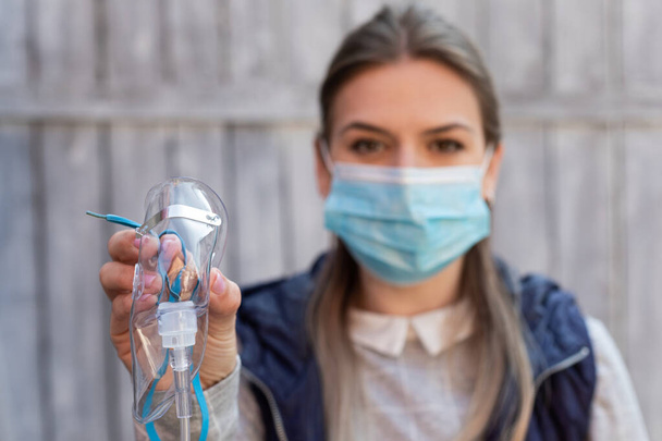 Woman wearing surgical mask is holding a medical oxygen mask outside - coronavirus pandemic - Foto, Imagen