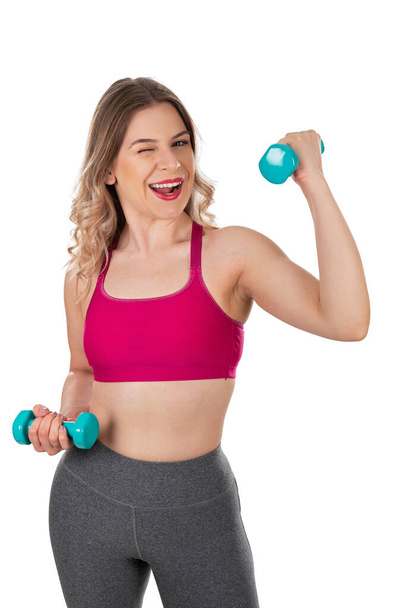 Attractive sporty woman holding  dumbbells is smiling to the camera on isolated background - Фото, изображение