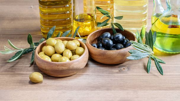 Green and black olives in the wooden bowls, olive oil bottles on the wooden background. Healthy mediterranean food.  - Zdjęcie, obraz