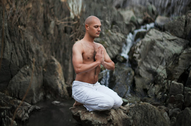 仏教。はげ男だ。滝を背景に山の中で瞑想。祈り. - 写真・画像