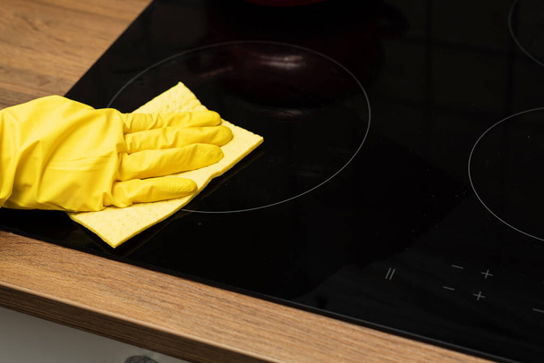 Someone is washing a kitchen stove in yellow gloves. Someone is cleaning a kitchen with rag in close view. - Photo, Image