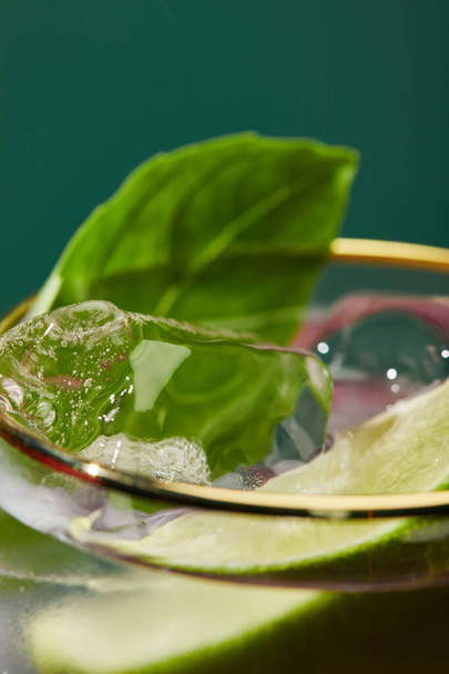 Vue rapprochée du verre recadré avec mojito rafraîchissant, menthe et tranche de citron vert isolé sur vert
 - Photo, image