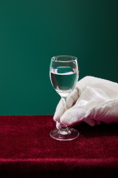 Vista recortada de la mano en guante de rizo sosteniendo vaso de chupito con líquido aislado en verde
 - Foto, imagen