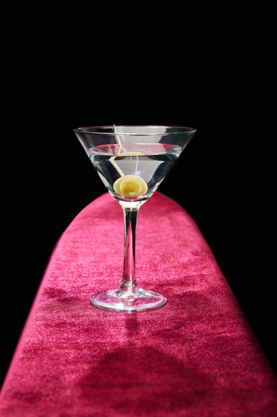 Cocktail glass with vermouth and whole olive on toothpick on pink surface isolated on black - Foto, Imagem