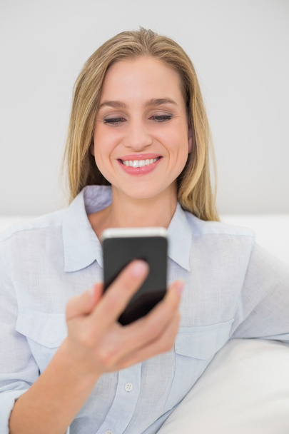Laughing casual blonde relaxing on couch holding smartphone - Фото, зображення