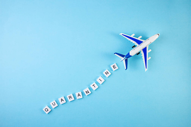 Το αεροπλάνο και η λέξη καραντίνα γραμμένα σε μπλε φόντο. Πανδημία Covid-19 Coronavirus καραντίνα έννοια. Η επιγραφή QUARANTINE με το μοντέλο αεροπλάνου - Φωτογραφία, εικόνα