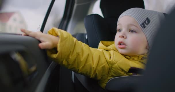 Boy looking the car window. Trip with family. Baby boy looking out of window car driving road trips travel. Medium shot of adorable toddler boy sitting in car seat of moving car and looking out window - Footage, Video