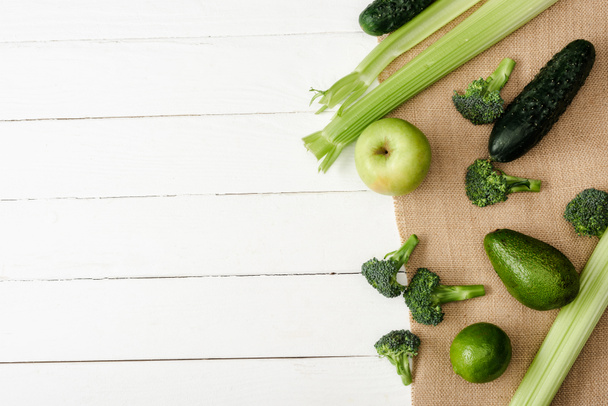 Taze yeşil meyve ve sebzelerin beyaz ahşap yüzeydeki çuval bezle üst görüntüsü - Fotoğraf, Görsel