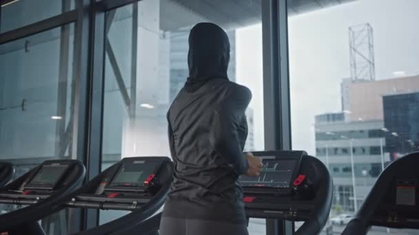 Athletic Muslim Sports Woman Wearing Hijab and Sportswear Running on a Treadmill. Energetic Fit Female Athlete Training in the Gym Alone. Urban Business District Window View. Back View Zoom in - Filmati, video