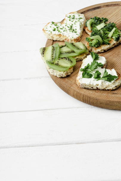 heart shaped canape with creamy cheese, broccoli, microgreen, parsley and kiwi on board on white wooden surface - Фото, изображение