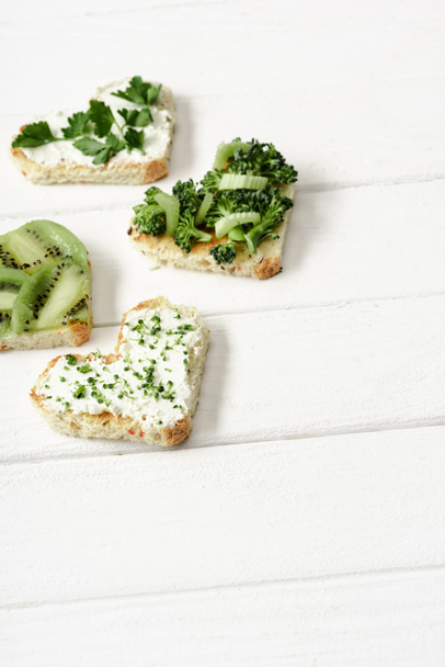 heart shaped canape with creamy cheese, broccoli, microgreen, parsley and kiwi on white wooden surface - Photo, Image