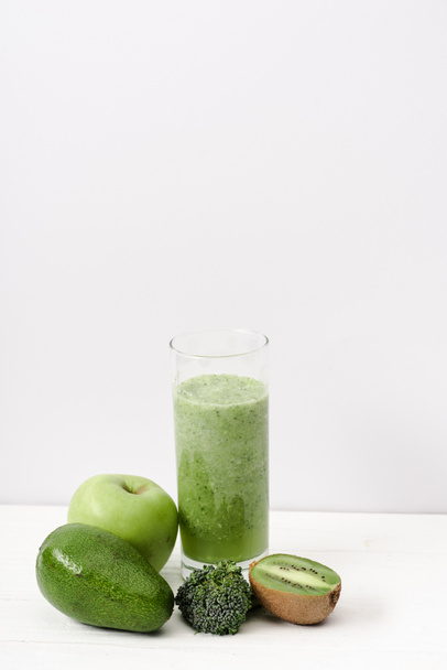 green smoothie in glass near kiwi, broccoli, avocado and apple on white wooden surface - Foto, Bild
