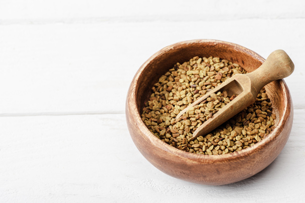 natural fenugreek in wooden bowl with spatula on white surface - Photo, image