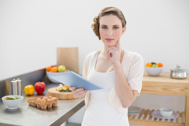 Thinking gorgeous woman standing in kitchen while holding her tablet - Foto, Bild