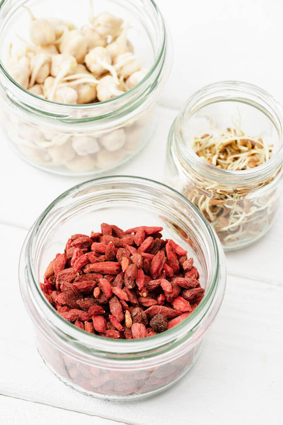 selective focus of goji berries and sprouts in glass jars on white wooden surface - 写真・画像