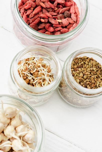 top view of goji berries and sprouts in glass jars on white wooden surface - 写真・画像