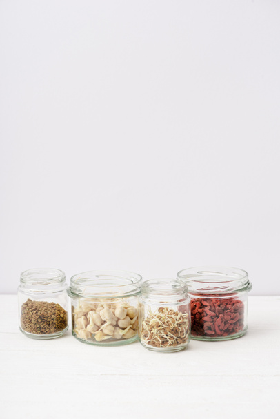 goji berries and sprouts in glass jars on white wooden surface - Photo, Image