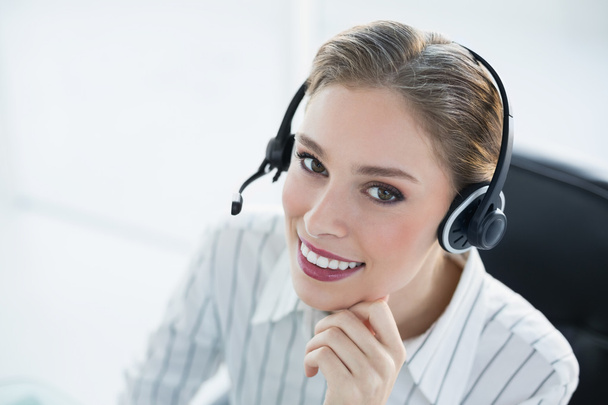 Beautiful smiling agent wearing headset sitting at her desk - Photo, image