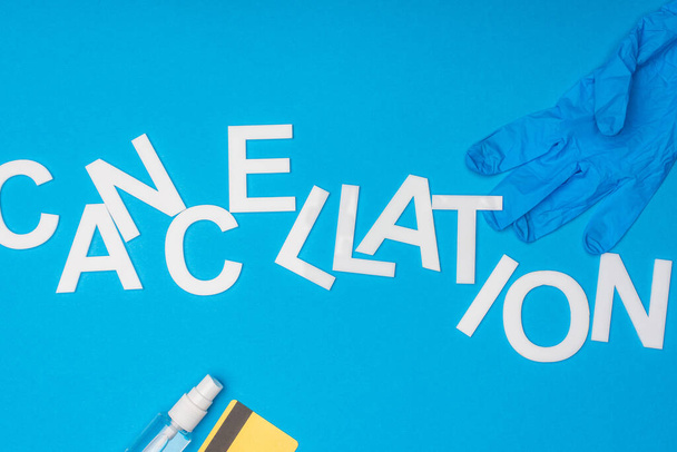 Top view of lettering cancellation with bottle of hand sanitizer, latex glove and credit card on blue background - Photo, Image