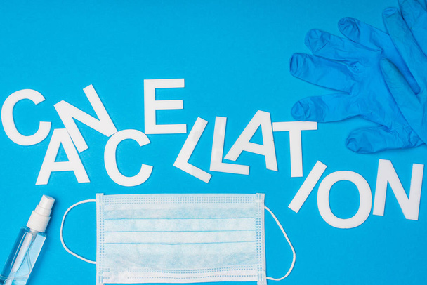 Vue du dessus de l'annulation de lettrage près du masque médical, bouteille de désinfectant pour les mains et gant en latex sur fond bleu
 - Photo, image