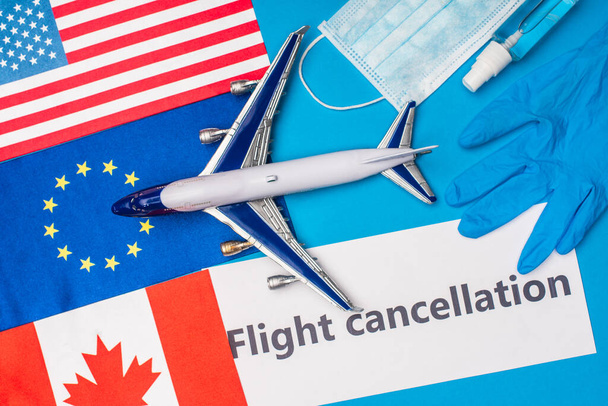 Vista dall'alto dell'aereo giocattolo, carta con iscrizione di cancellazione del volo vicino alla maschera medica e bandiere dei paesi sulla superficie blu
 - Foto, immagini