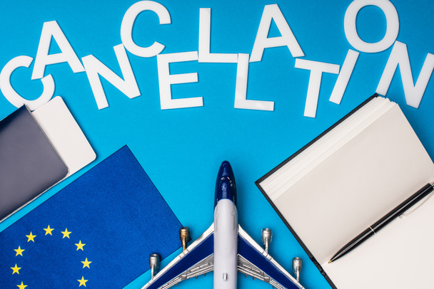 Top view of lettering cancellation near toy plane, flag of european unity and passport with air ticket on blue background - Photo, Image