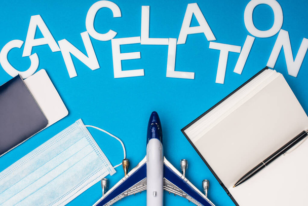 Top view of toy plane, medical mask with notebook and cancellation lettering on blue background - Foto, Imagem