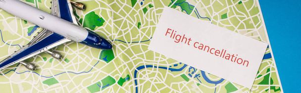 Top view of card with flight cancellation near toy plane on map isolated on blue, panoramic shot - Photo, Image