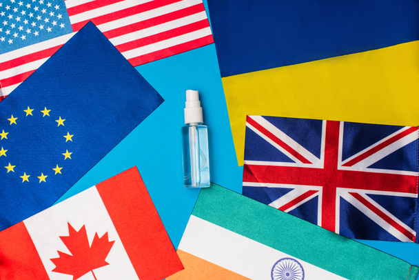 Vista superior de la botella de desinfectante de manos cerca de banderas de países sobre fondo azul
 - Foto, Imagen