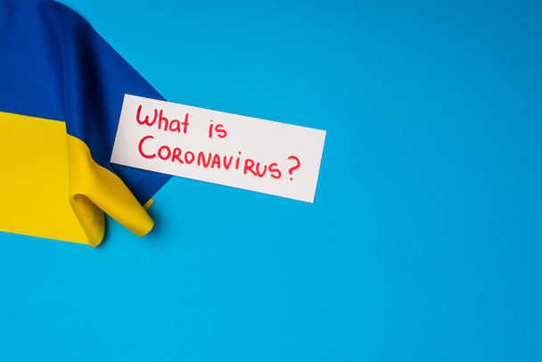 Horní pohled na kartu s tím, co je koronavirus písmo v blízkosti vlajky ukrajinské na modrém pozadí - Fotografie, Obrázek