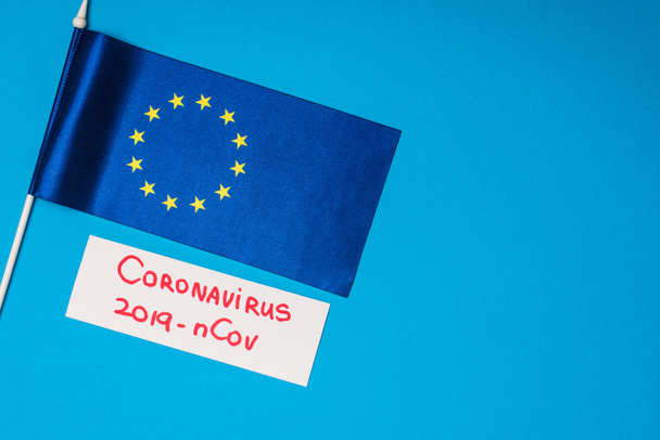 Top view of flag of european unity and card with coronavirus 2019-nCov lettering on blue background - Foto, Imagem