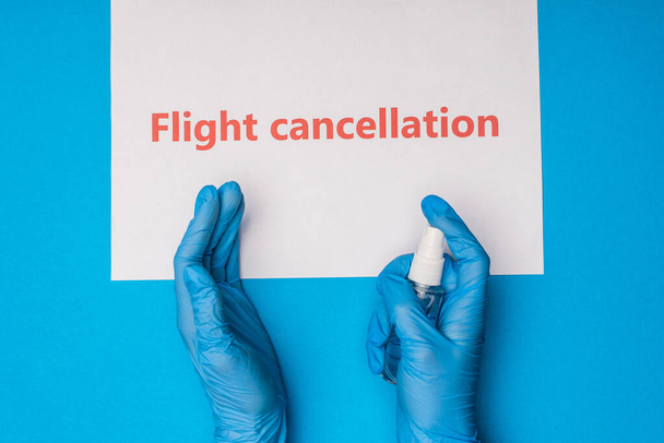 Top view of doctor holding bottle of hand sanitizer near card with flight cancellation lettering on blue background - Fotoğraf, Görsel