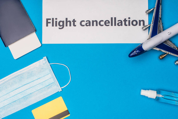 Vista superior de la tarjeta con letras de cancelación de vuelo, máscara médica, tarjeta de crédito y avión de juguete sobre fondo azul
 - Foto, Imagen