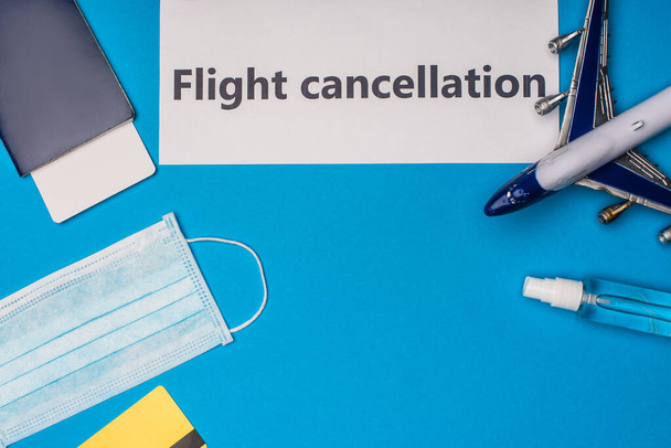 Vista superior de la tarjeta con letras de cancelación de vuelo cerca de máscara médica, avión de juguete, pasaporte y billete de avión sobre fondo azul
 - Foto, Imagen