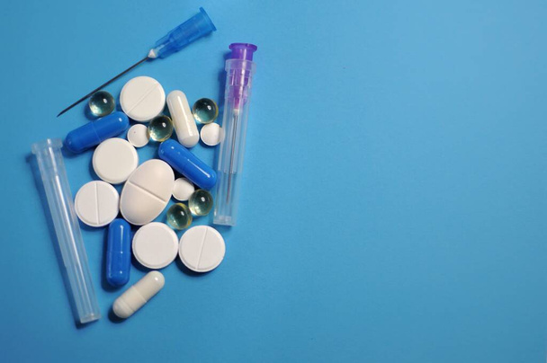 Veel verschillende pillen met spuit op blauwe tafel. Veel kleurrijke verschillende pillen, waaronder anti-virale medicijnen. Geneesmiddelen tegen COVID-19 en andere ziekten - Foto, afbeelding